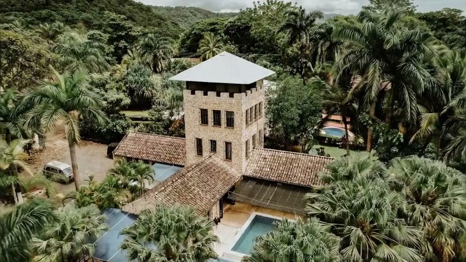 Concept aerial approach toward Castillo's stone tower, pools, and tropical grounds.